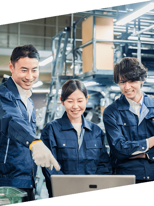 工場内で作業着を着たスタッフがパソコン画面を囲み、情報を共有している様子